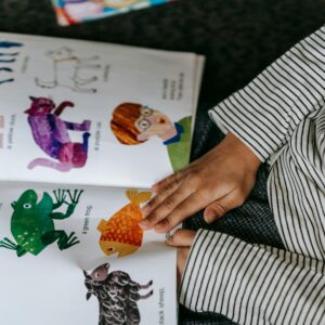 From above of crop anonymous child reading interesting book with colorful pictures of different animals